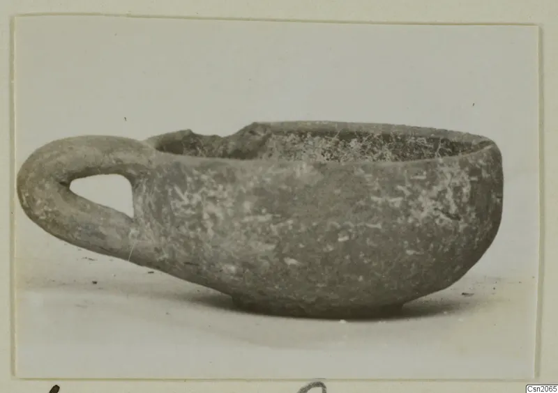 Small pottery bowl with a single loop handle, seen from the side.