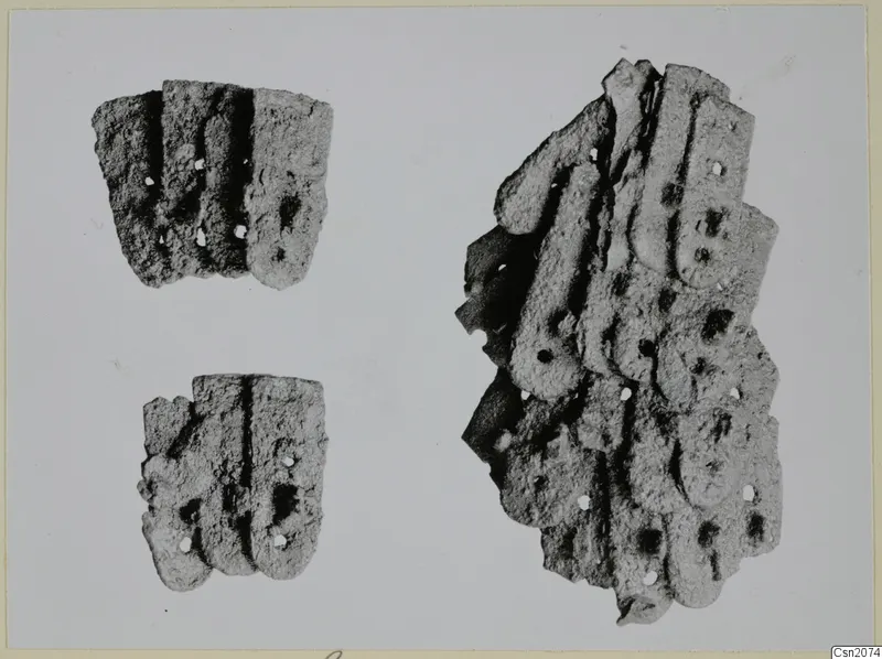 Three corroded iron fragments with raised parallel ridges and small round holes, on a plain pale background.