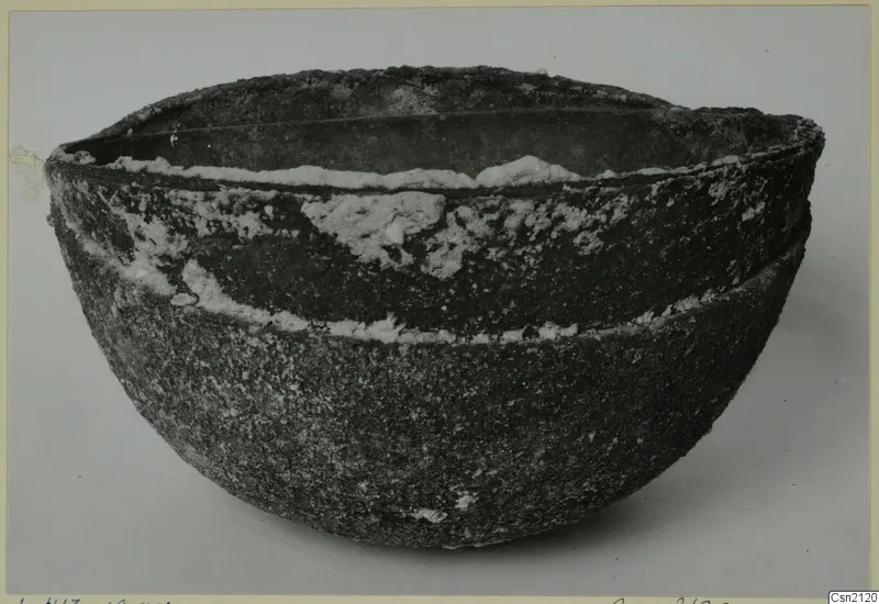 Large heavily corroded metal bowl with encrusted white deposits, photographed on a plain grey background.