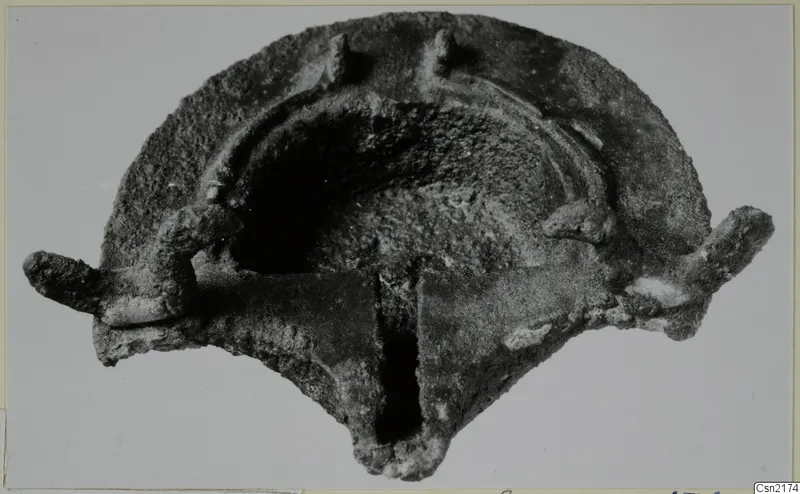 Corroded metal lamp with a rounded body, a central hollow and projecting lugs, shown alone on a plain background.