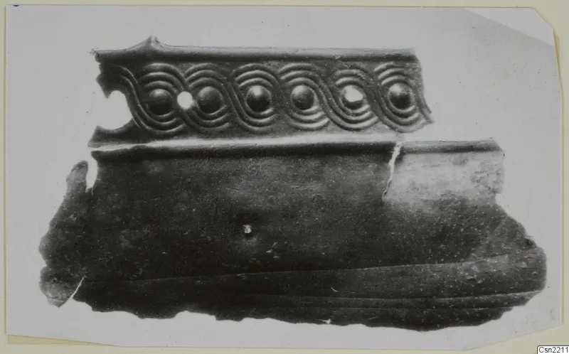 Bronze mounting fragment with a relief band of spiral scrolls enclosing round bosses, on a plain white background.