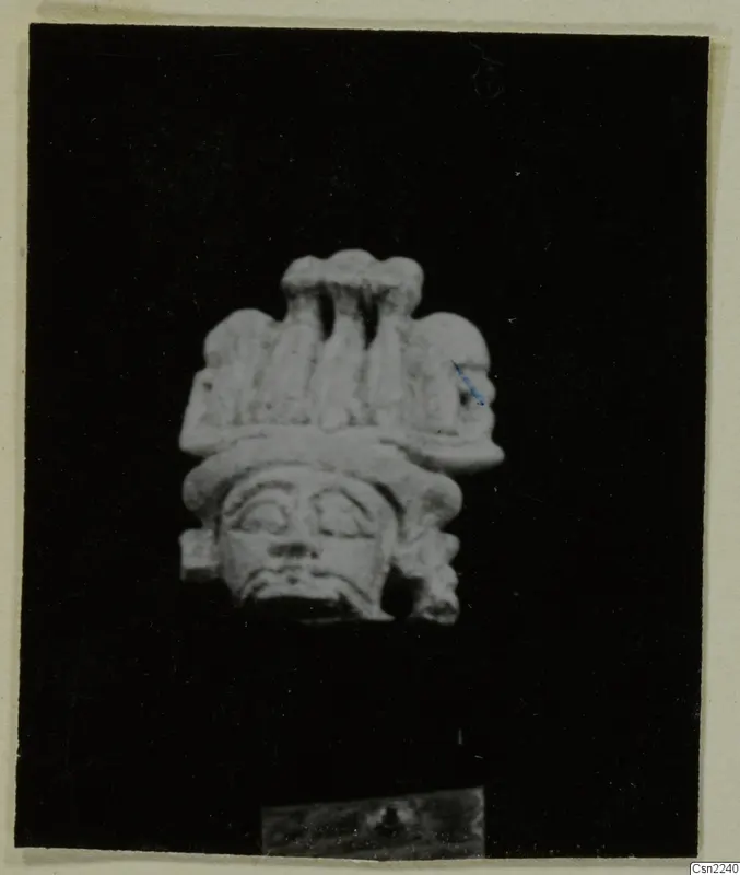 Pale carved head with a tall lobed headdress, photographed against a black background
