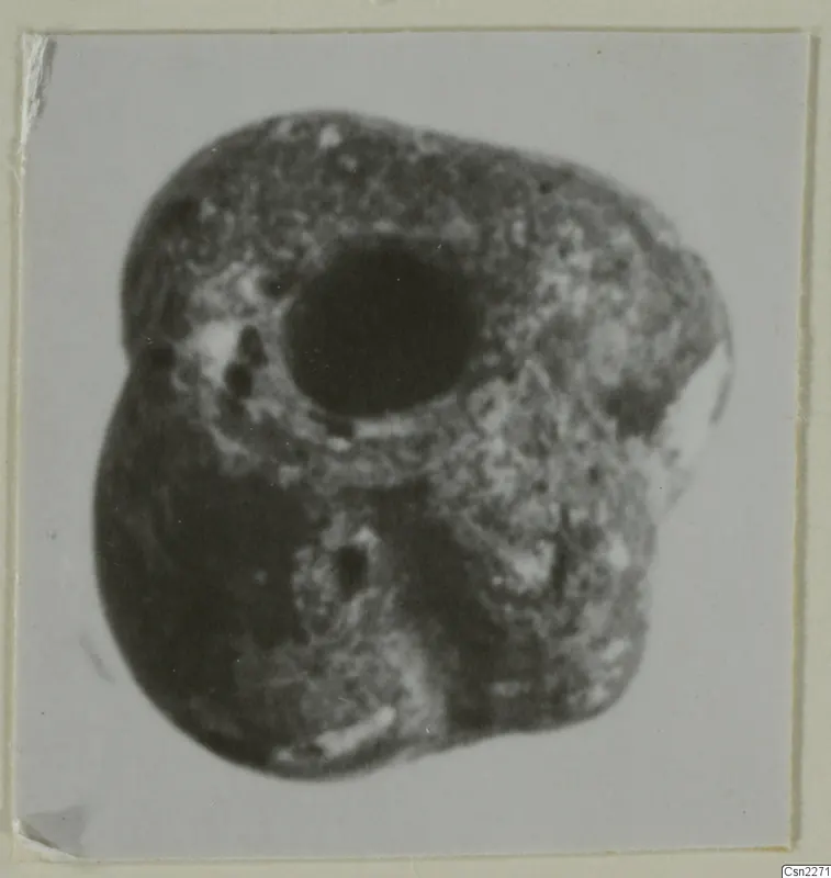 Blurred close-up photograph of a lumpy dark object with a large round hole, from Idalion