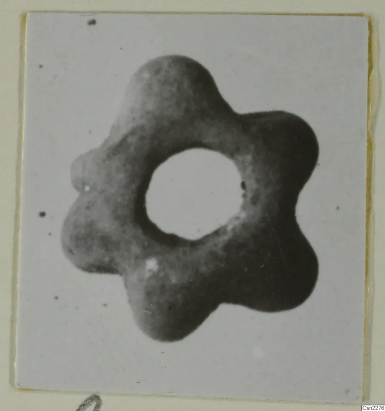 Six-lobed ring-shaped object with a large central hole, grey in colour, shown close up