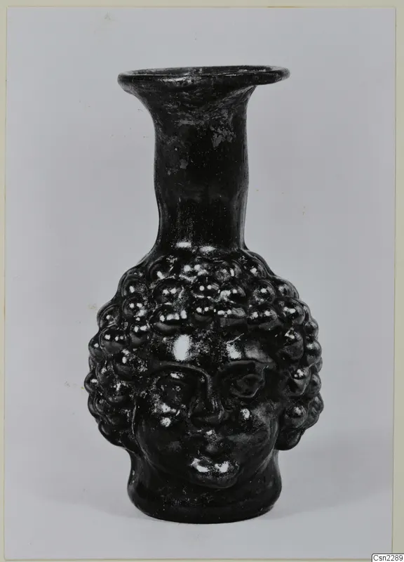 Dark glass flask shaped as a head, with bead-like curls of hair and a tall flared neck