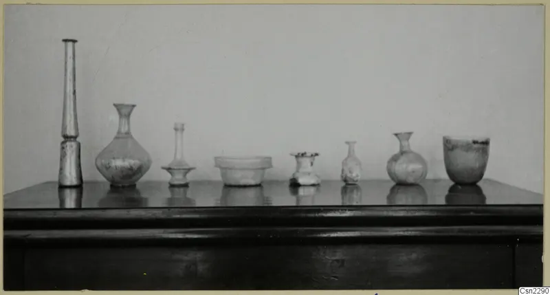 Seven blown glass vessels of varied forms standing in a row on a dark wooden table.