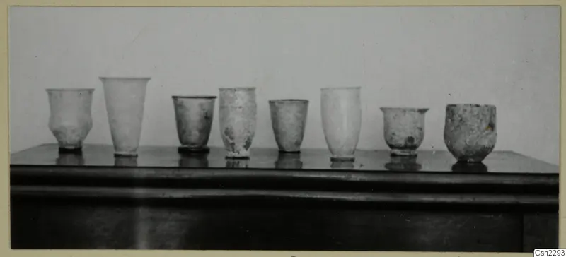 Row of several blown glass vessels standing on a dark wooden surface, Vouni