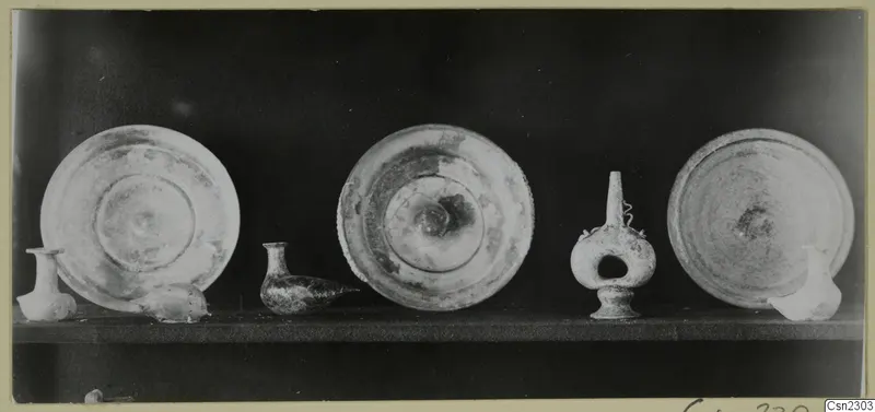 Three shallow dishes and several small vases standing in a row on a shelf against a dark background