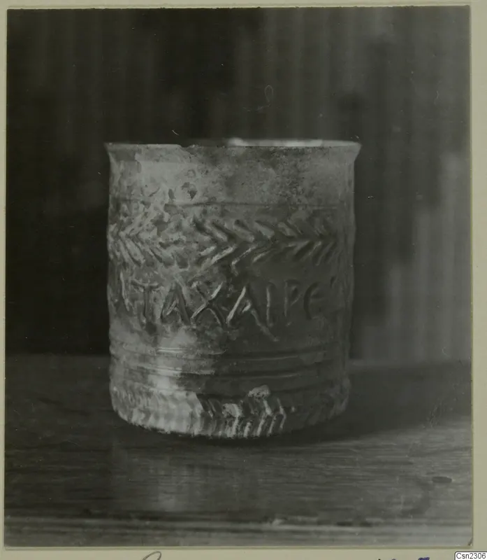Small straight-sided cup with raised lettering and chevron bands, standing on a wooden surface