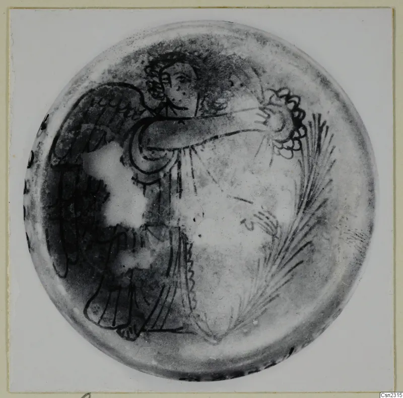 Blown glass object seen from above, decorated with dark painted lines of a winged figure and feathery fronds
