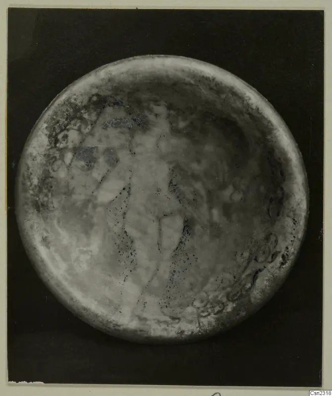 Blown glass object seen from above, with a faint upright pattern across its round surface.