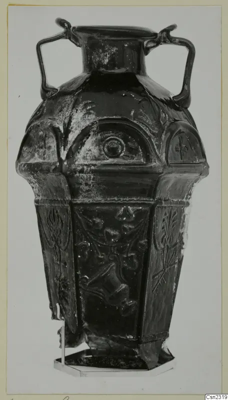 Blown glass vessel with two handles, a faceted body and raised relief decoration, standing on a metal stand