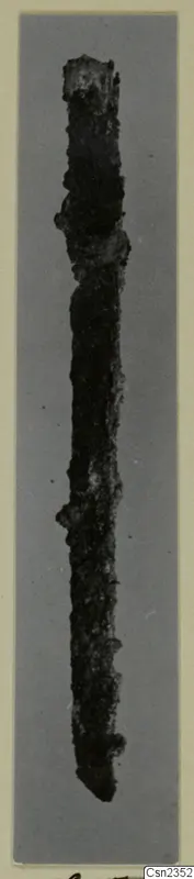 Corroded iron knife, upright against a grey background, shown on a photo mount.