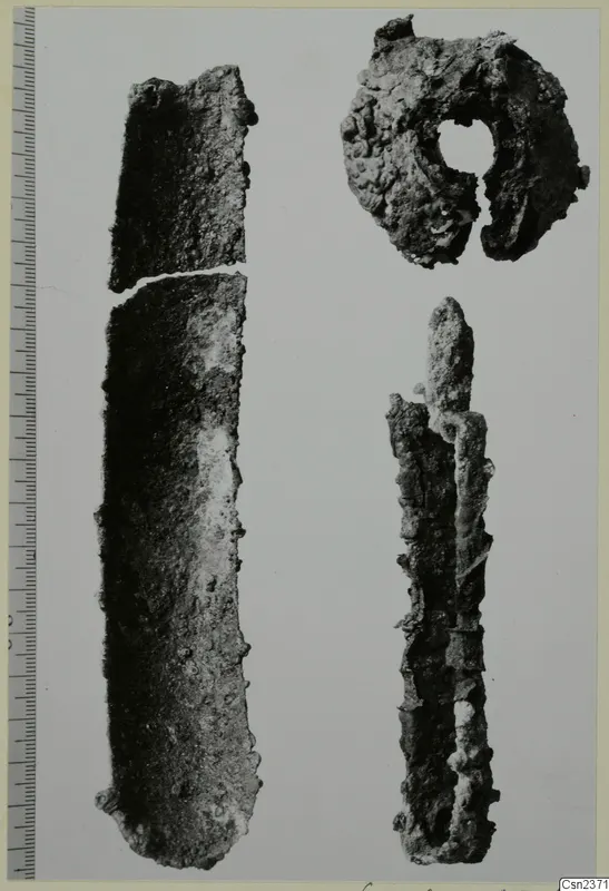 Three corroded iron objects: a long flat blade broken in two, a ring-shaped piece, and a narrow split object, with a scale bar at left.