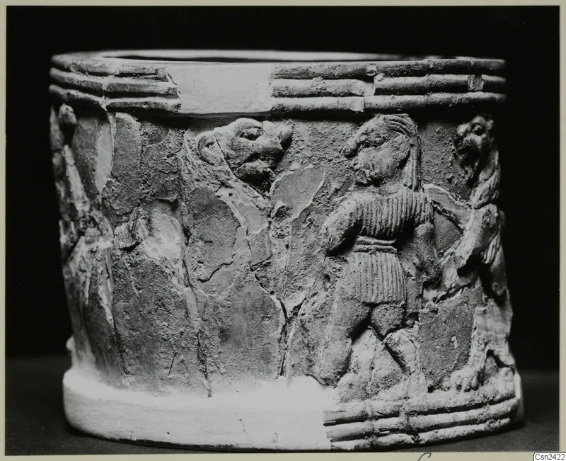 Cylindrical object with figures carved in relief on its side, showing a standing figure and an animal head