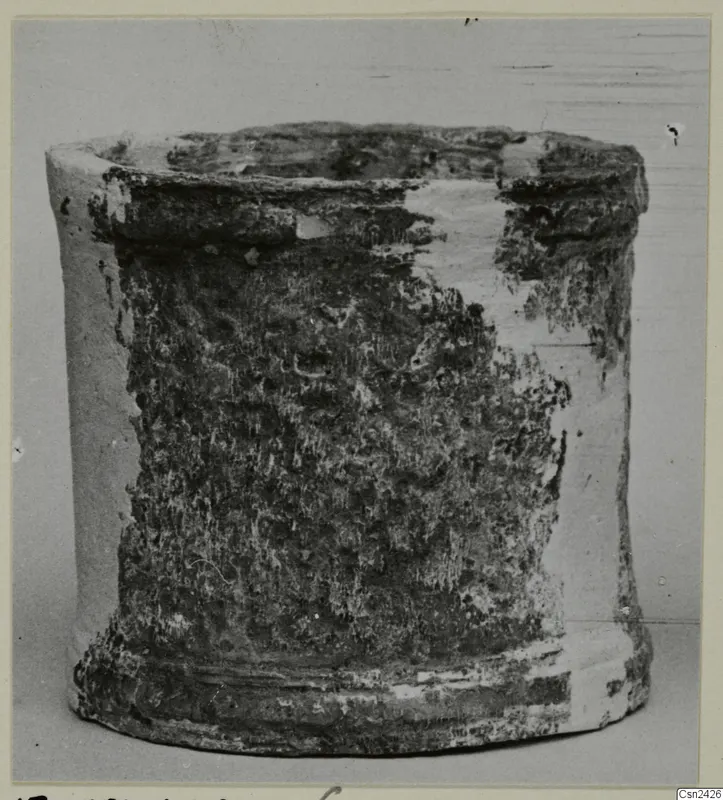 Cylindrical object with an open top and flared base, pale surface partly covered by dark encrusted deposits