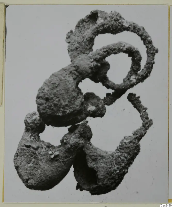 Corroded silver object, a tangle of loops and lumpy forms, shown against a plain pale grey background.