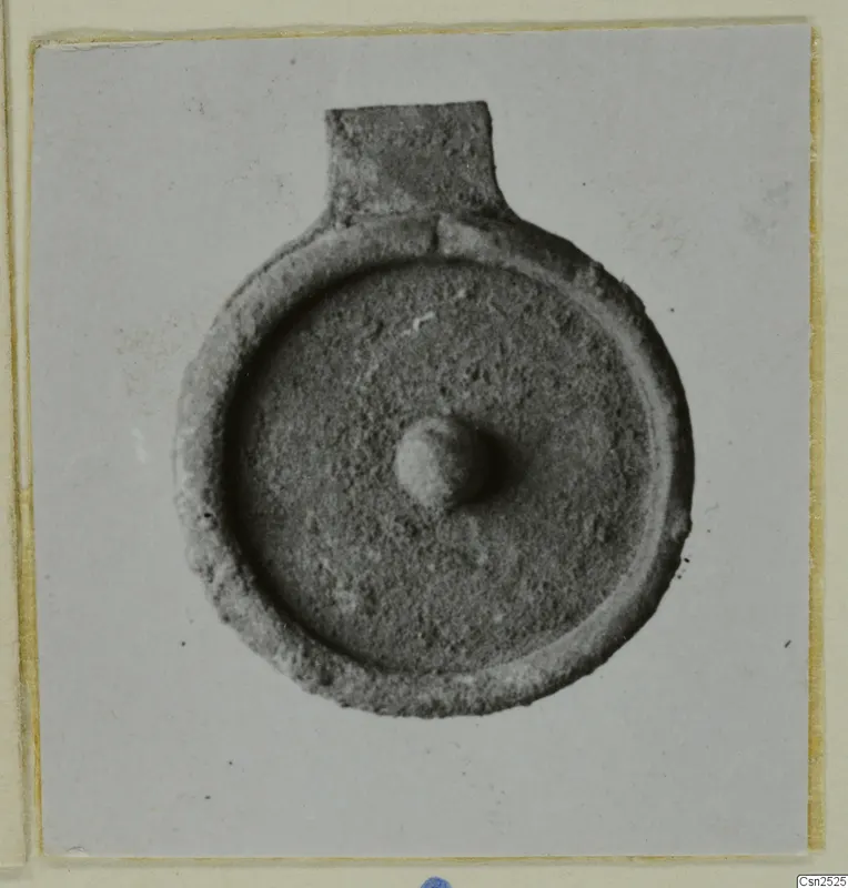 Silver find: a round flat object with a raised rim, a rectangular tab at the top and a small central knob