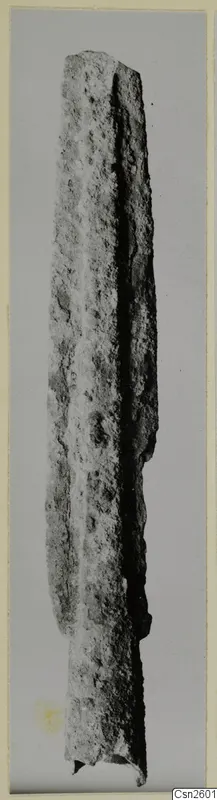 Corroded bronze weapon, a long blade, from the Amathus tombs 1–9 series, photographed upright.
