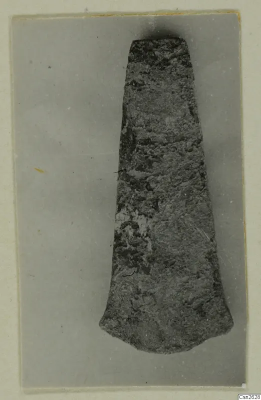 Corroded flat metal blade or axe-head from Lapithos, photographed on grey card.