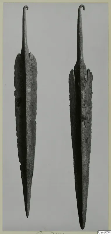 Two long corroded metal blades with hooked tangs, shown side by side against a grey background