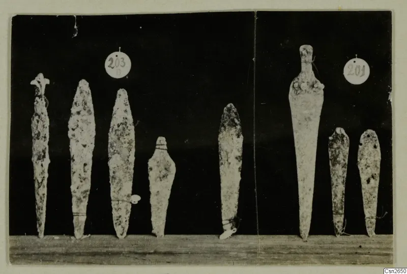 Seven narrow metal blades standing upright on a wooden board, with two round number labels behind them