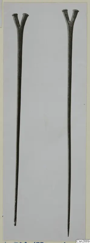 Two long bronze rods with forked, Y-shaped tops, photographed side by side on a pale grey card.