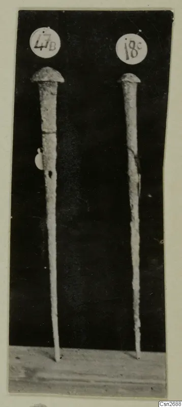 Two long metal tools with domed heads standing upright, each marked with a round number label