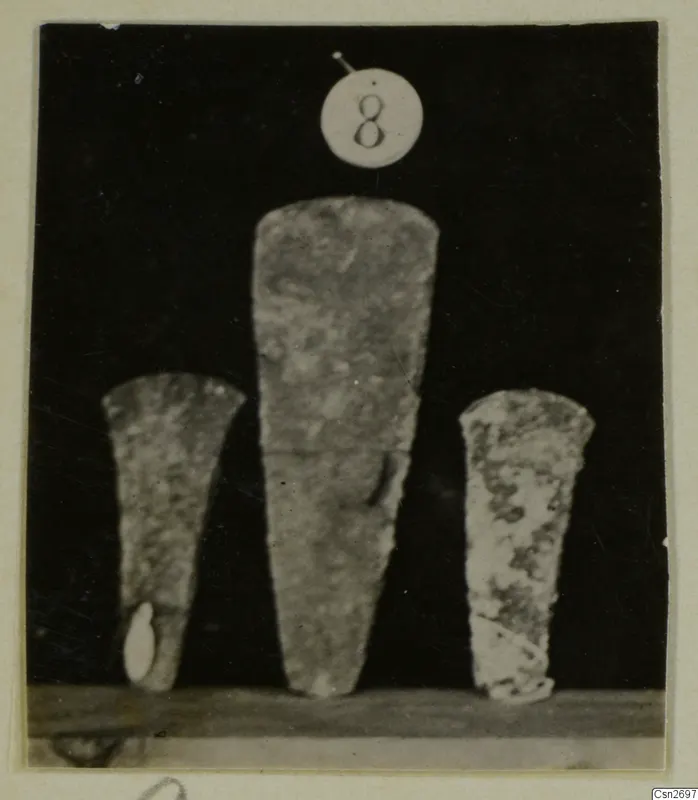Three tapering tools standing upright on a shelf against a dark background, recorded as bronze tools