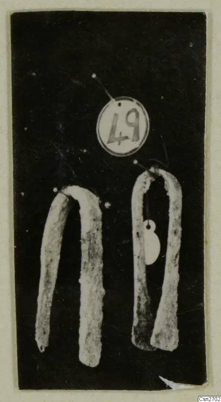 Two bent bronze tools on a dark background, with a round number label above them