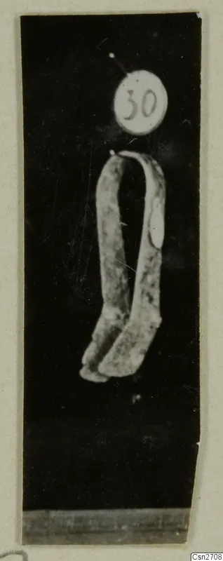 Bronze tool: a bent metal object with two arms joined at the top, photographed against black with a number label above it.