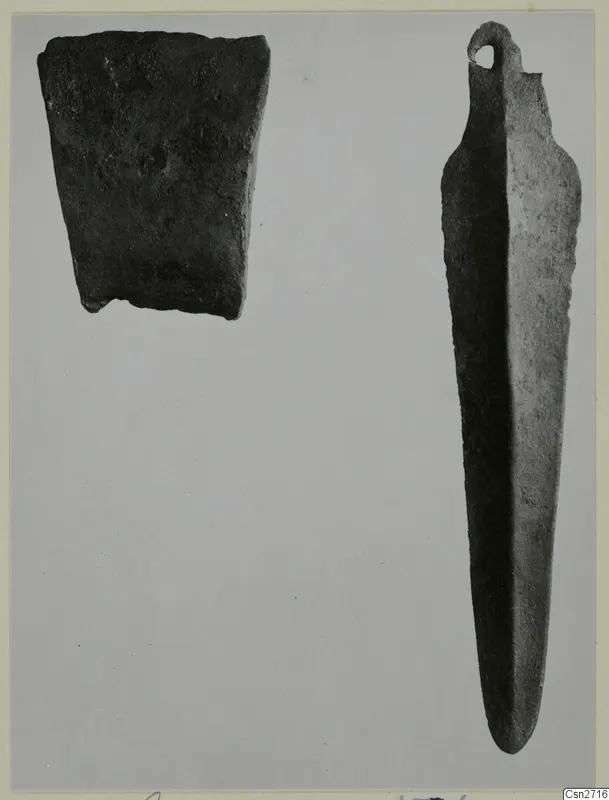 Two bronze tools on a grey background: a corroded rectangular fragment and a long, narrow tool with a loop at one end.