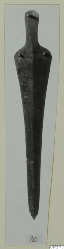 Long tapered bronze tool with a rounded top and two rivet holes at the shoulders