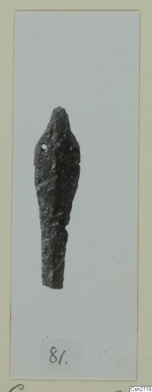 Corroded bronze tool with a small hole near its upper end, shown on a mounted card.