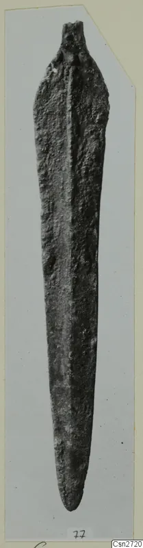 Corroded bronze blade with a short tang, photographed upright on a grey card mount.