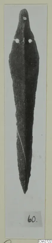 Long narrow bronze blade with a pointed tip and two rivet holes near the top, photographed on a card mount