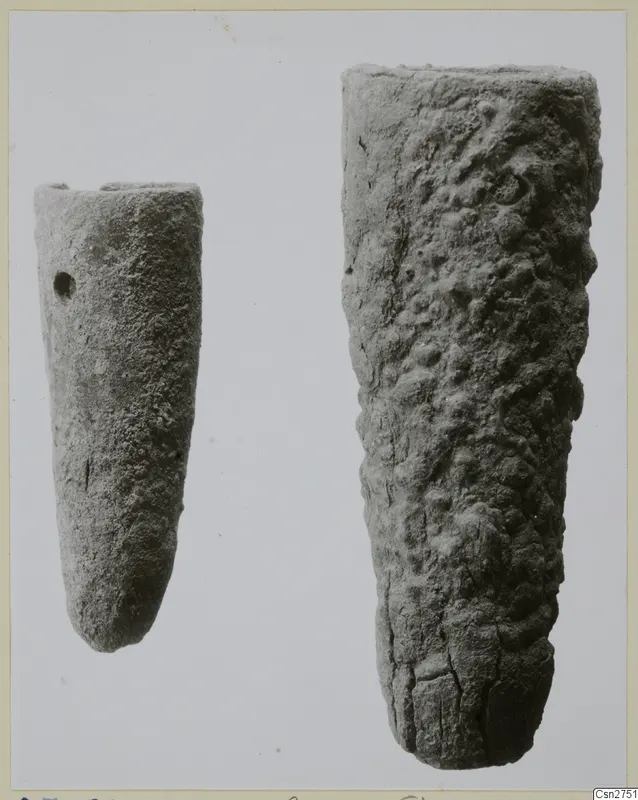 Two tapering bronze tools side by side, the smaller one with a small hole near its top, the larger one with a pitted, knobbly surface.