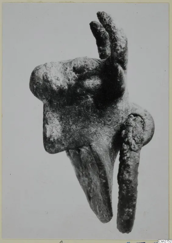 Corroded metal object with two upright prongs, a long downward-curving projection and a rod, on a pale background