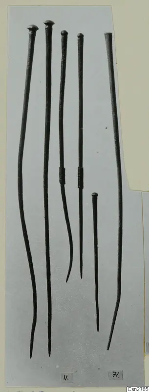 Five long bronze tools with knobbed heads and pointed tips, laid out on a grey background