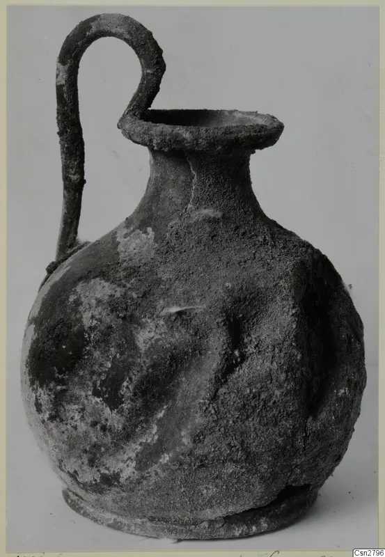 Bronze jug with a looped handle and a flared mouth, its surface encrusted with corrosion.