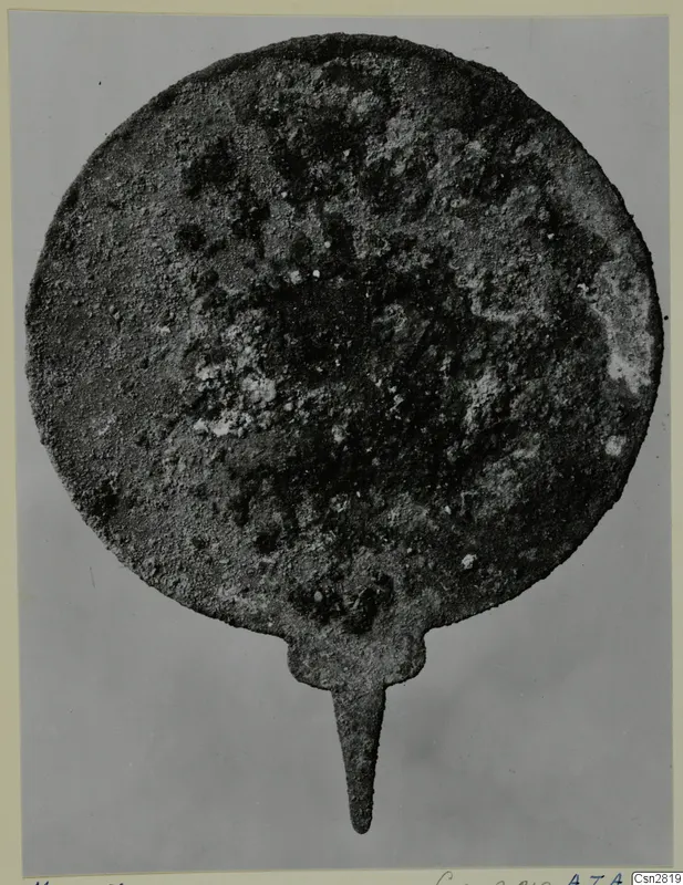 Corroded round bronze object with a narrow tang, from the Marion tomb finds (toilet-requisites)