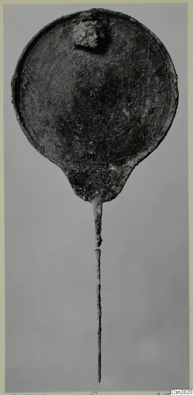 Bronze mirror with a round disc and long thin handle, photographed against a grey background