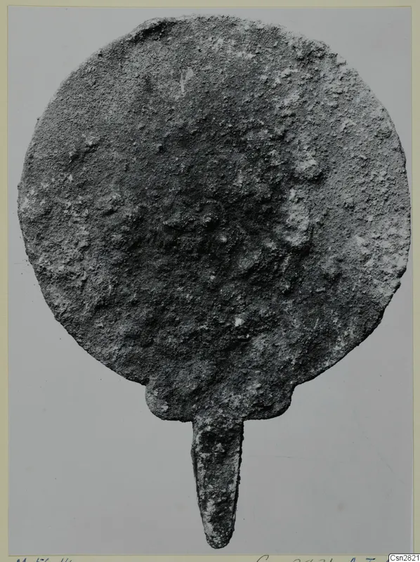 Corroded bronze disc with a tapering tang, one of the toilet requisites from the Marion tombs