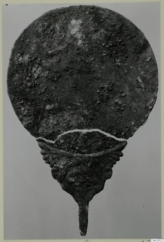 Bronze mirror from Marion with a round, corroded disc and a handle topped by a face in relief