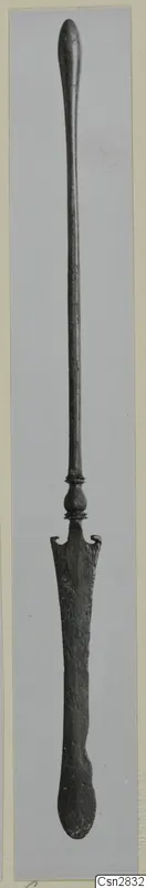 Long bronze implement with a rounded top end, a knob collar and a flat, spatula-like blade at the lower end.