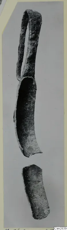 Corroded bronze strigil with a loop handle and a separate curved fragment below