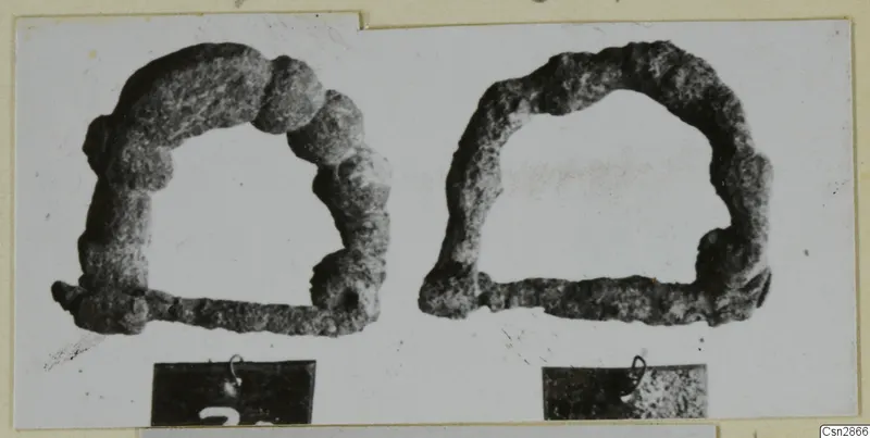 Two corroded metal arched objects with straight bars, shown side by side on a card mount.
