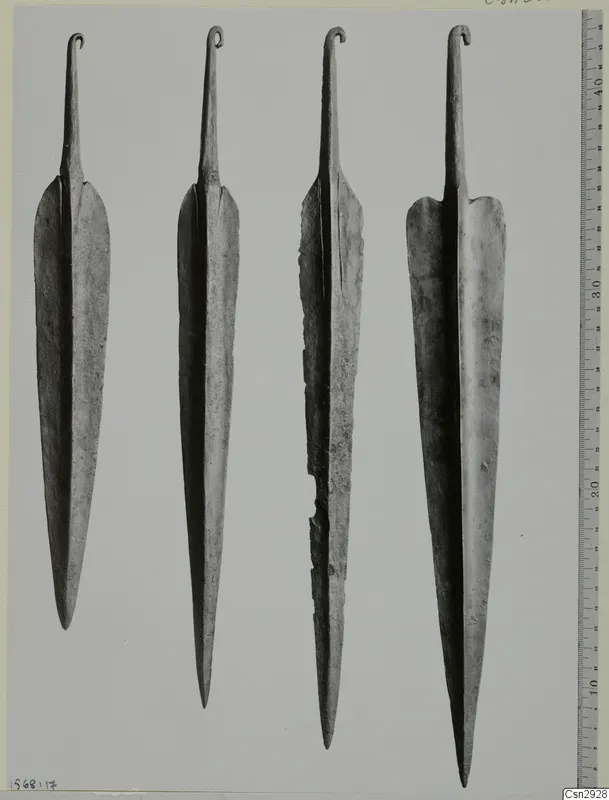 Four long metal blades with hooked tangs at the top, photographed side by side beside a measuring ruler