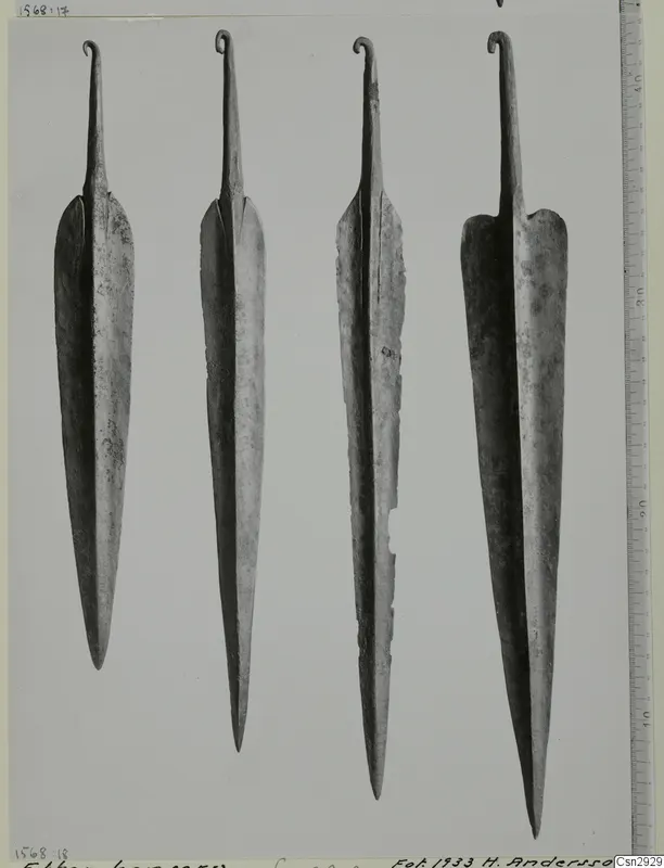 Four metal blades with pointed ends and curled hooked tangs, set upright side by side on a grey background.