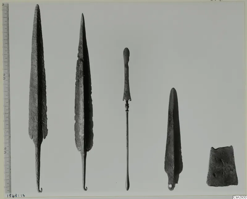 Five corroded metal points and implements set in a row beside a measuring scale